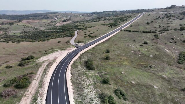 Otlak ve çalılık arazide uzanan, beyaz şeritli yeni asfalt yolun havadan görüntüsü.