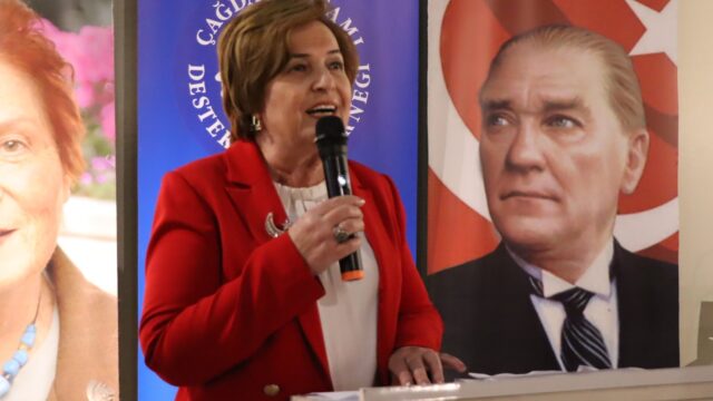 Kırmızı ceketli bir kadın mikrofonla konuşuyor; arkasında ÇYDD pankartı ve Atatürk portresi bulunuyor.