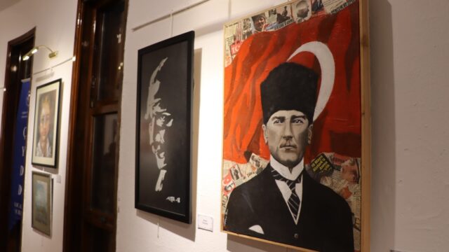 Galeri duvarında Türk bayrağı fonlu Atatürk portresi ve yanında siyah beyaz bir portre tablosu asılı.