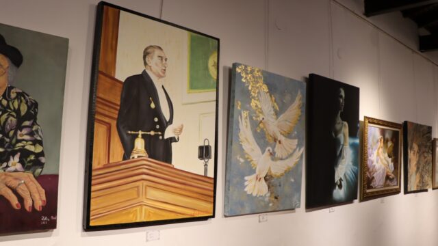 Galeri duvarında kürsüde konuşan Atatürk tablosu, yanında güvercin resmi ve diğer tablolar sergileniyor.