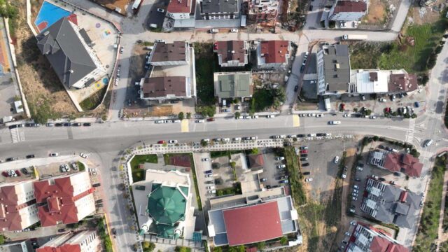 Tam tepeden çekilmiş hava görüntüsünde yatay bir cadde, yeşil kubbeli cami ve çevresindeki binalar.