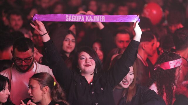 Siyah ceketli genç kadın, üzerinde Sagopa Kajmer yazan mor bir bandı iki elle yukarı tutuyor.