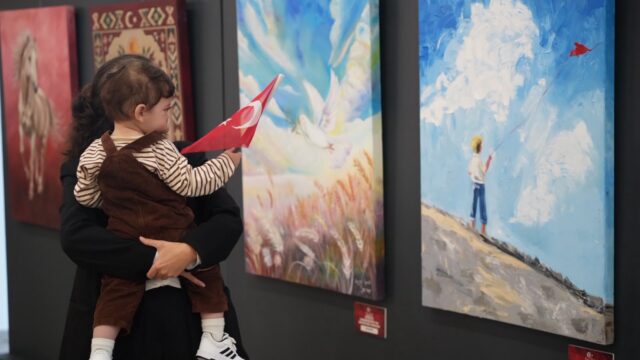 Kucakta taşınan bir bebek, elindeki Türk bayrağıyla sergideki tablolara bakıyor.