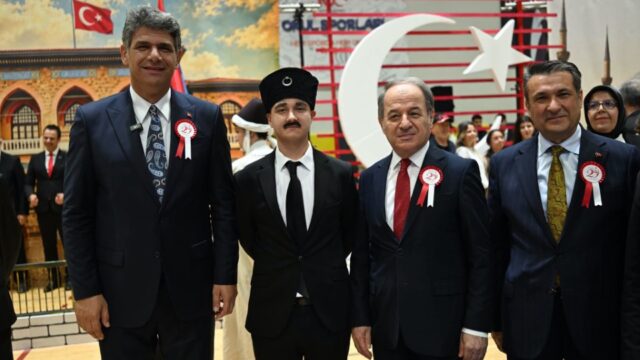 Üç takım elbiseli yetkili ile siyah kalpaklı genç bir sahne oyuncusu kameraya poz veriyor.
