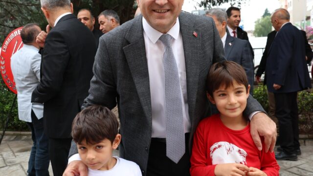 Gözlüklü bir adam, Atatürk baskılı tişörtler giyen iki erkek çocuğun omzuna sarılmış, kameraya gülümsüyor.