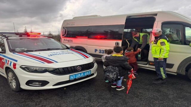 Trafik jandarması personeli, yanıp sönen ışıklı aracın yanında servis minibüsünden inen öğrencileri kontrol ediyor.