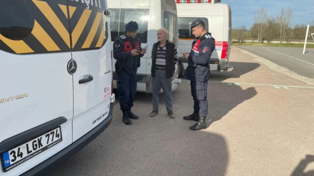 İki jandarma personeli, okul servis araçlarının yanında yaşlı bir erkek sürücüyle konuşuyor.
