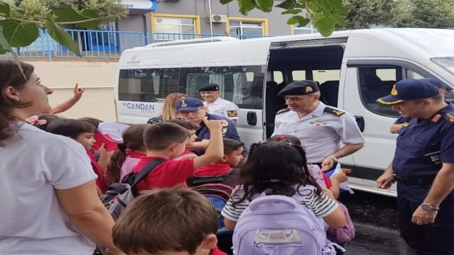 Servis minibüsünün önünde jandarma personeli ve okul çocukları ile bir kadın bir arada duruyor.