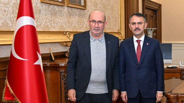 Makam odasında, Türk bayrağı ve iki portrenin önünde koyu takım elbiseli iki erkek yan yana poz veriyor.